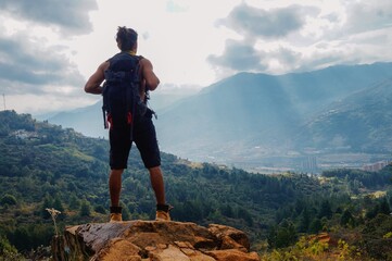 Young man standing with long hair without shirt and big backpack on rock in the mountain looking...