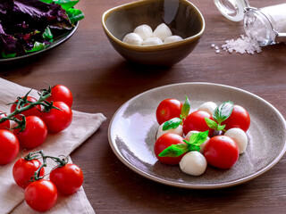 Caprese salad on round plate. Round tomatoes, mini mozzarella and green basil.