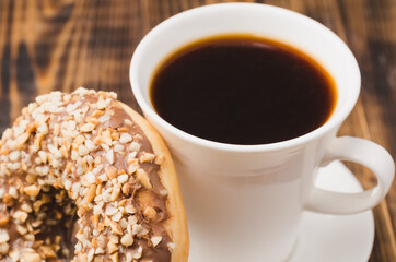 White cup of black coffee and donut with nuts.