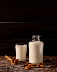 Almond milk in a bottle and a glass, on dark vintage wooden background, with copy-space