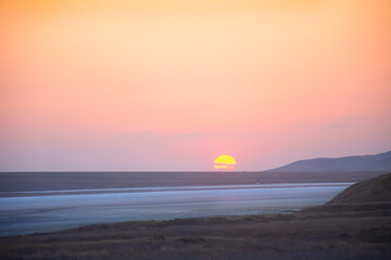 Colorful sunset over a plain with a salt lake and hills on the horizon