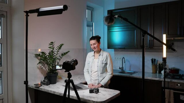 Woman blogger or vlogger streaming online on social media to her subscribers. Woman using microphone, video camera and other blogging set ups at her house while talking on camera.