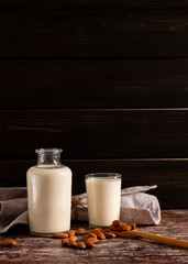 Almond milk in a bottle and a glass, on dark vintage wooden background, with copy-space