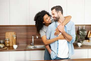 Close-up of a happy interracial couple standing in the kitchen, happy romantic owners of a new flat...