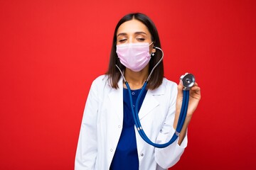 Photo of professional confident young european female doctor in medical mask and white coat, stethoscope over neck, ready help patient, fight disease