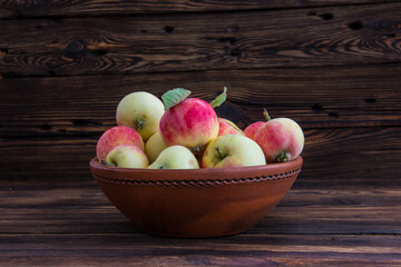 A clay bowl with apples on a wooden table.