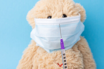 Teddy bear wearing protective medical mask looking to the syringe with Covid-19 vaccine. Coronavirus vaccination