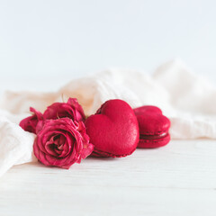 Heart-shaped macaroons with pink rose on a white wooden background. Concept for Valentine's Day.