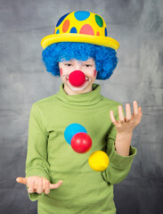 Fototapeta na wymiar young child dressed as a clown with wig and fake nose has fun playing with colorful balls celebrating carnival