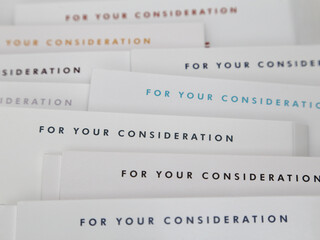 A pile of DVD movie and TV show screener jackets displaying FOR YOUR CONSIDERATION is shown up close. FYC is an advertising heading soliciting awards votes from entertainment industry guild members.