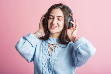 Joyful brunette girl listens to music on headphones in the studio on a pink background