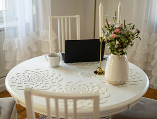 Home office. Laptop standing on the white round table. Beautifull bouquet of flowers and candles.