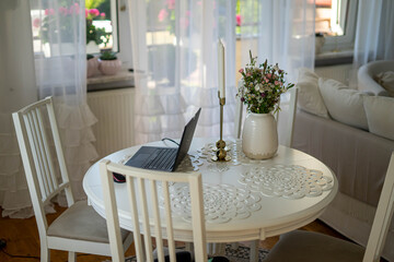 Home office. Laptop standing on the white round table. Beautifull bouquet of flowers and candles.