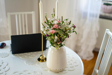 Home office. Laptop standing on the white round table. Beautifull bouquet of flowers and candles.