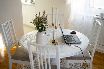 Home office. Laptop standing on the white round table. Beautifull bouquet of flowers and candles.