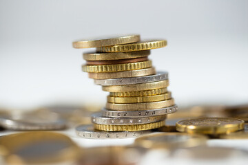 Metallic euro coins standing in a pile with abundance of others lying around on white table. Detailed close-up of cash standing in a column. Concept of earning interest and finance.