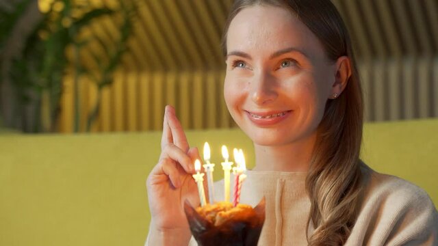 Woman makes a wish, blows out the candles on a birthday cake and laughs