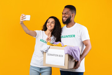 Two Volunteers Making Selfie With Donation Box Over Yellow Background