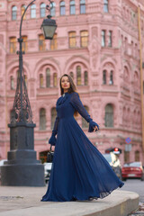 Naklejka premium Elegant caucasian woman with long straight brunette hair in blue and white stylish colorful dress walking city street on a bright day