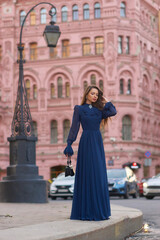 Elegant caucasian woman with long straight brunette hair in blue and white stylish colorful dress walking city street on a bright day
