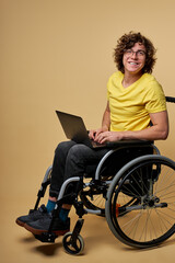 man disabled student preparing for exam using laptop, sitting on wheelchair isolated in studio. portrait. online education for handicapped people