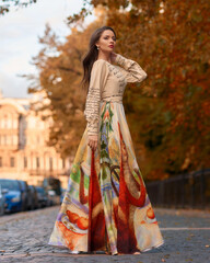 Elegant caucasian woman with long straight brunette hair in bright stylish colorful dress walking city street on a bright day