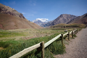 Fototapeta na wymiar Wooden fence along hiking trail in Aconcagua National Park with view to snow caped highest mountain Andes - Aconcagua peak. Andes Mountains, Mendoza province, Argentina