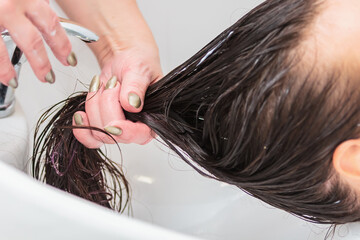 The hairdresser washes the head of a girl with long hair in the sink.
