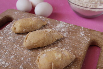 Raw cooking dumplings lie on a board beside egg flour on a pink background view from above