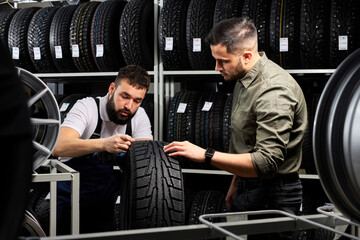 auto mechanic talk about advantages of auto tire to young client in service, man came to buy new...