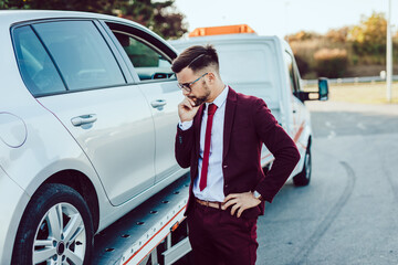 Elegant middle age business man waiting for towing service for help on the road. Roadside assistance concept.