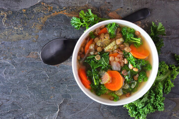 Healthy vegetable soup with kale and lentils. Top view scene on a dark slate background.