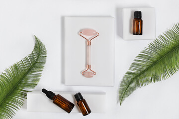Pink quarts face massage jade roller with cosmetic massage oil on white background top view.