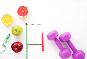 Naklejka na ściany i meble Notepad, dumbbells, fruits on a white isolated background. Healthy lifestyle, diet and results. Top view, flat lay