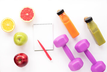 Fototapeta na wymiar Notepad, dumbbells, fruits, smoothies on a white isolated background. Healthy lifestyle, diet and athletic performance. Top view, flat lay