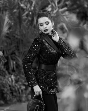 Woman In Black Sequin Blazer Posing Against Exotic Trees On Background