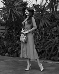 Full-body portrait of woman in knitted dress and hat posing in glasshouse
