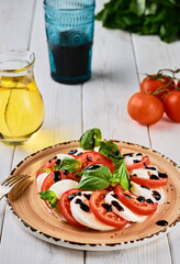 Italian Caprese salad with tomatoes, mozzarella cheese, basil balsamic vinegar and olive oil. On a ceramic plate on a white wooden table. Country style. Vegetarian dish