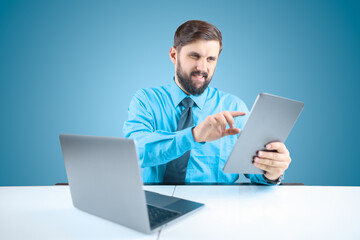 a solid man in an office at a computer holds a tablet in one hand and clicks on it when performing financial reports