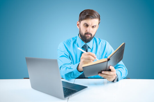a solid man in an office at a desk writes down financial transactions in a notebook