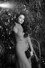 Long-haired woman in gray knitted dress standing against tropical trees on background