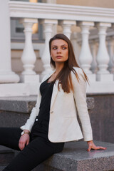 Young woman in black shirt, jeans and white blazer walking and posing outdoors on a summer day. Sun backlight. Outdoor portrait