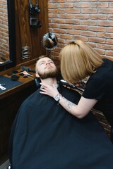 Professional hairdresser woman doing styling of handsome guy with electric hair clipper at barber shop