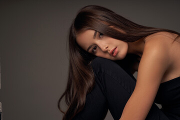 Fototapeta premium Close-up breast-up portrait of young beautiful brunette teenager girl with long straight hair and perfect natural make-up posing against grey background