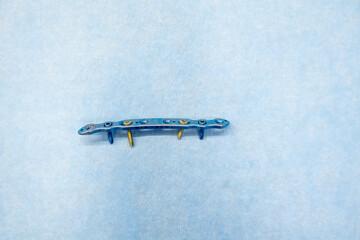  explanted titanium plate and 4 titanium screws for the treatment of a clavicle fracture lie on a light blue support