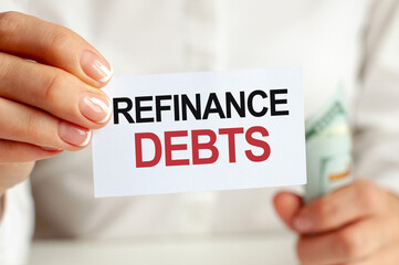 On the table are bills, a bundle of dollars and a sign on which it is written - REFINANCE DEBTS. Finance and economics concept.