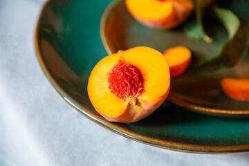Peach in half with bone. Rustic minimalist food peach fruits with leaves on green plate on tablecloth. Harvest of Ripe juicy peaches. Still life Peaches fruit