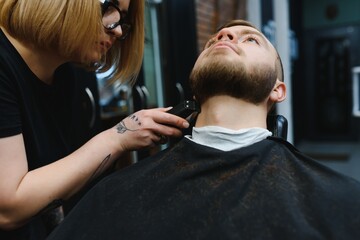 Barbershop or hairdresser concept. Woman hairdresser cuts beard with scissors. Man with long beard, mustache and stylish hair. Guy with modern hairstyle visiting hairdresser