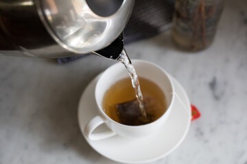 Pouring boiling water from jug into tea cup