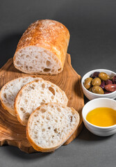 Traditional Italian ciabatta with olives and olive oil on a wooden board on the table. Craft bread and healthy food concept